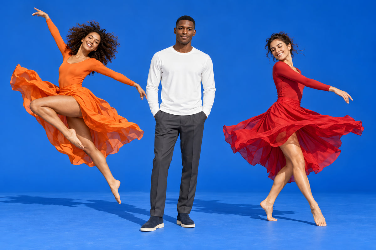 Un homme en t-shirt blanc entre deux danseuses en orange et en rouge, sur fond bleu